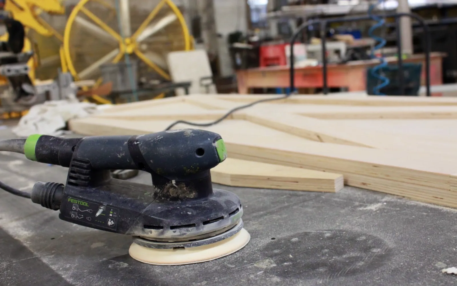Orbital sander rests beside cut timber on a workshop bench