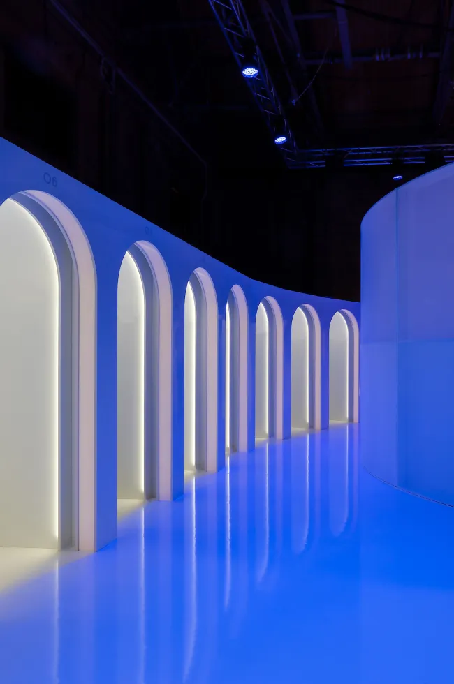 Curved corridor lined with blue-lit arched fitting rooms
