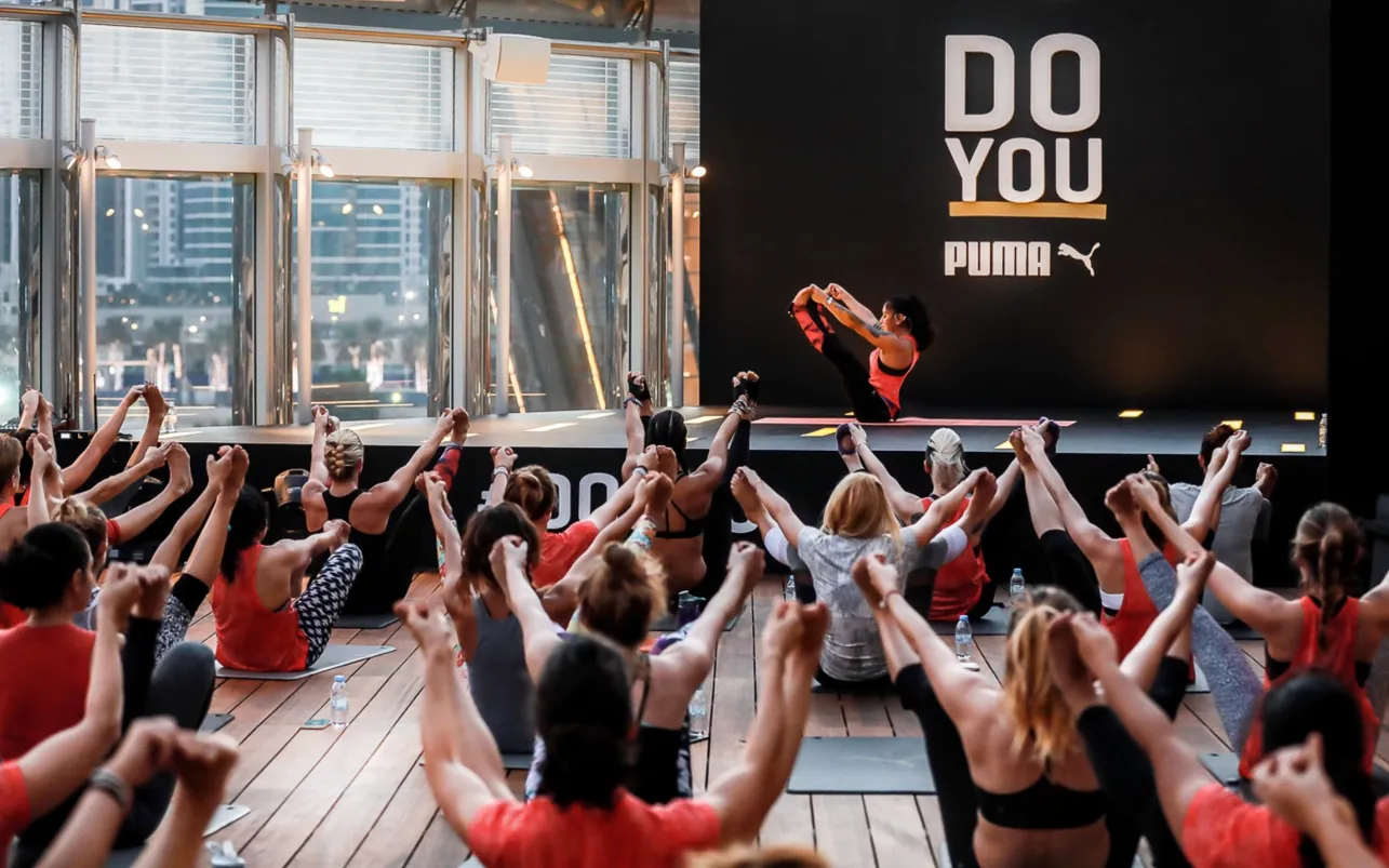 Instructor leads a group stretch before the large Puma backdrop