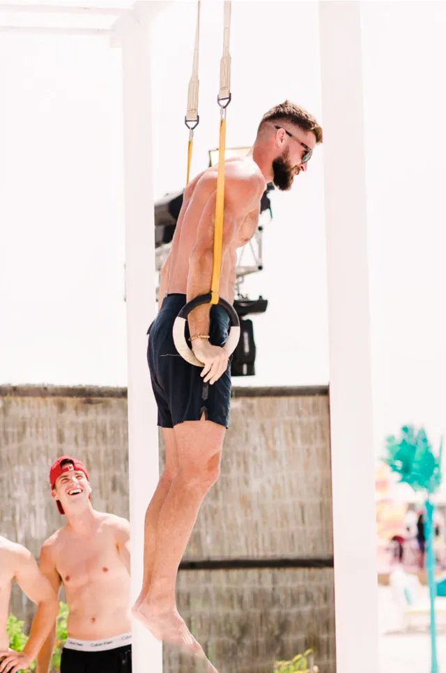 Athlete exercises on suspended rings while another guest watches