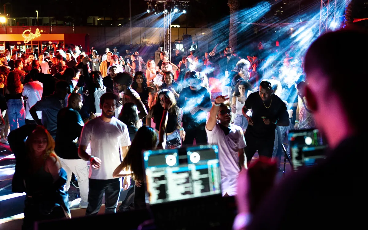 Festival crowd dances beneath sweeping stage lights at night