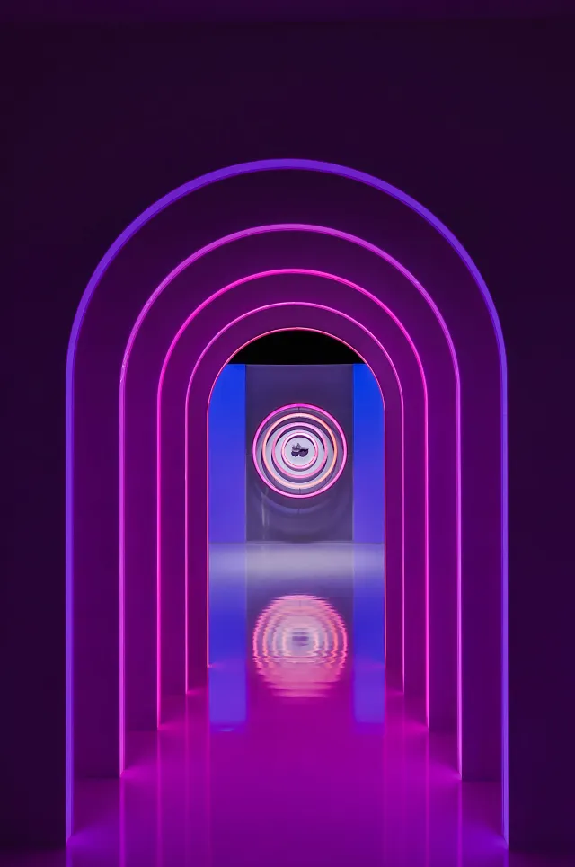 Nested neon arches reflect along the dark exhibition corridor