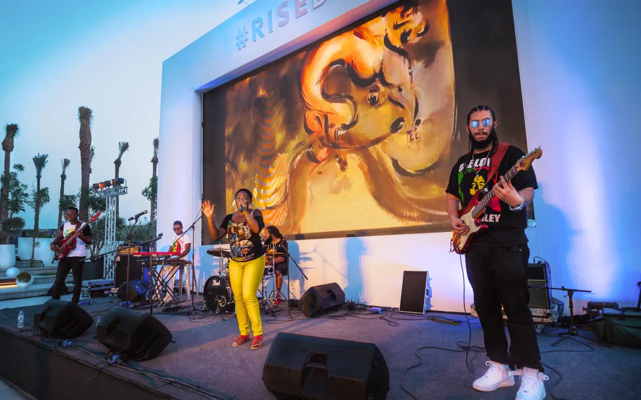 Live band performs before a large art screen on the outdoor stage