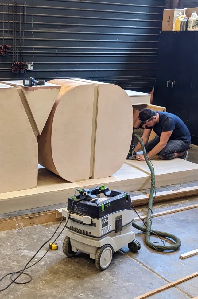 Fabricator shapes oversized wooden letters inside the workshop