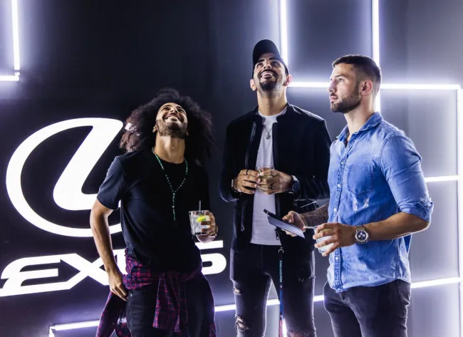 Three guests socialize beside the illuminated Lexus backdrop