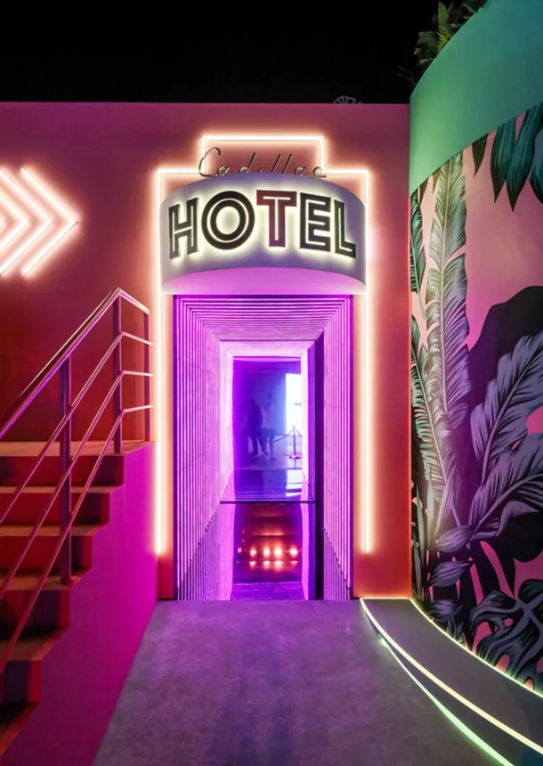 Neon Cadillac Hotel entrance framed by tropical murals and pink lighting