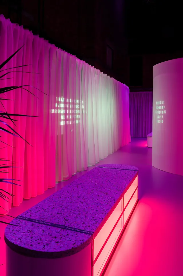Curved speckled bench beside pink-lit translucent changing-room curtains
