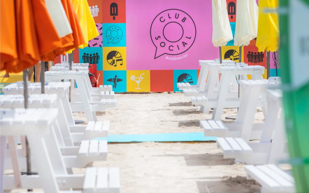 White picnic tables and umbrellas fill the colorful beach festival venue