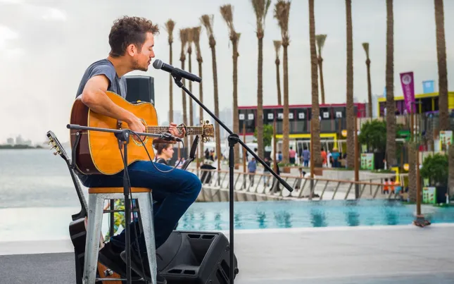 Acoustic guitarist performs beside a pool and palm-lined promenade