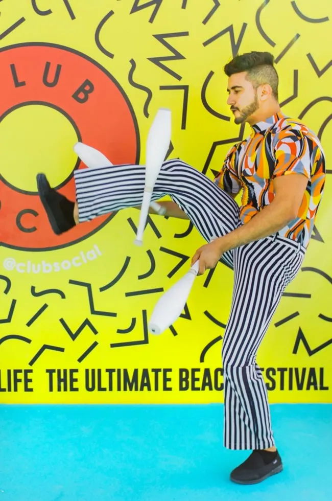 Juggler performs with white clubs against a colorful Club Social mural