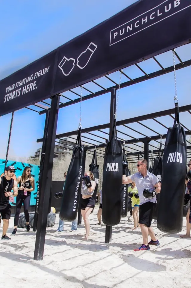 Guests train at an outdoor boxing bag station on the beach
